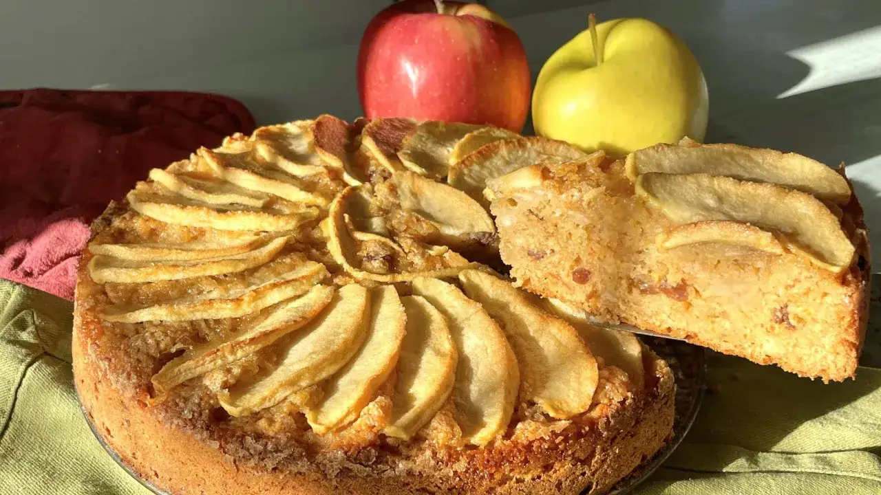 Una deliziosa torta di pane e mele alla trentina, con mele fresche sullo sfondo.