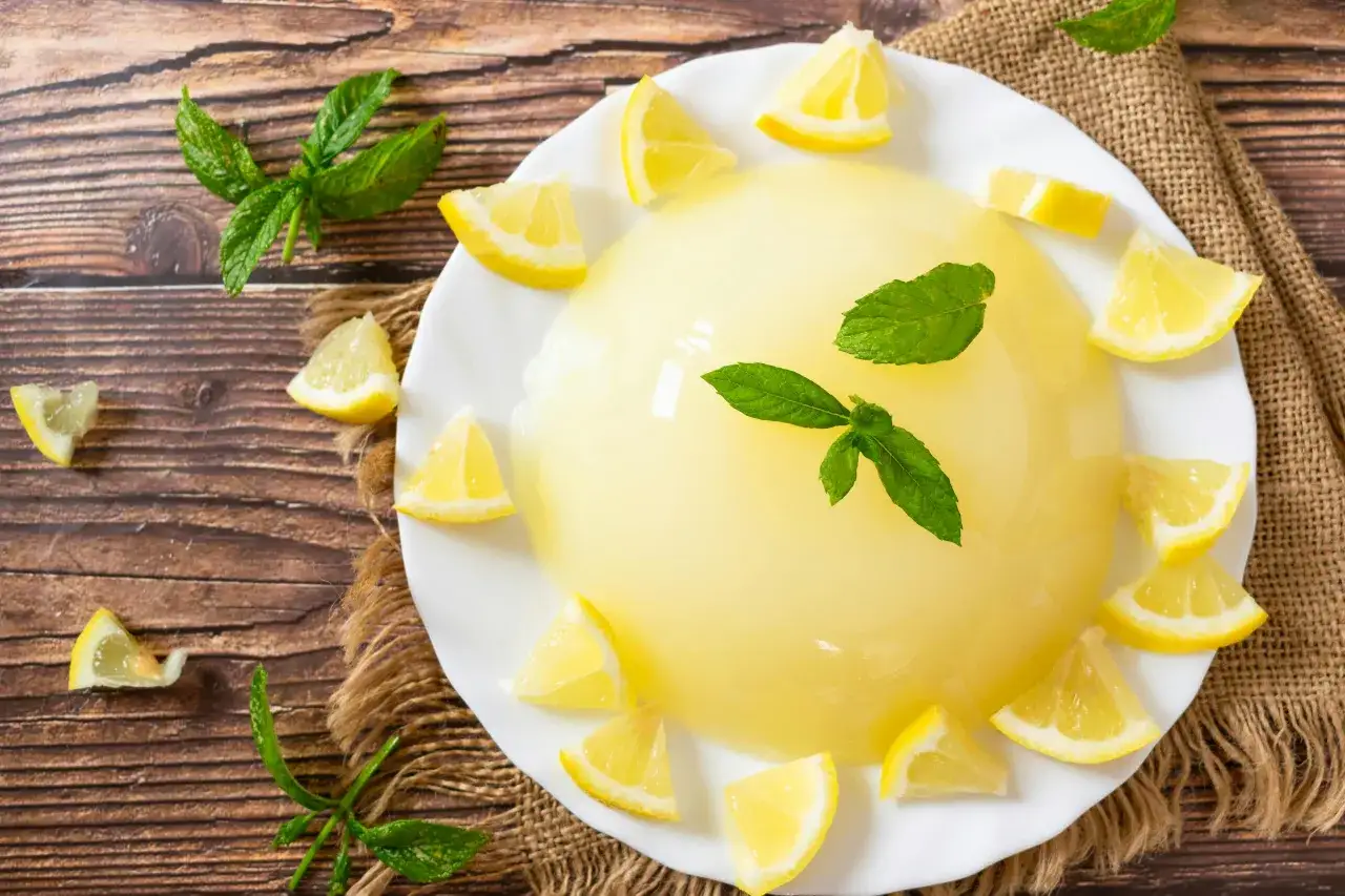 Un delizioso gelo di limone, guarnito con spicchi di limone fresco e foglie di menta, su un piatto bianco, su uno sfondo di legno rustico.
