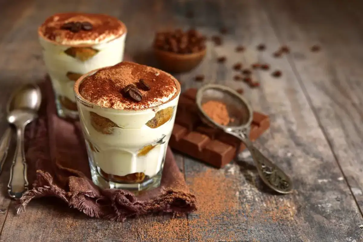Delizioso tiramisù con ricotta, strati di savoiardi e crema al caffè, spolverato di cacao e chicchi di caffè.