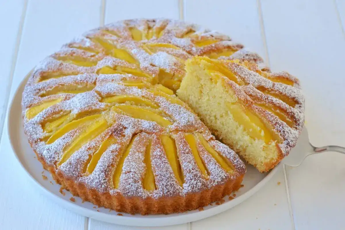 Deliziosa cheesecake al mango, con fette di mango disposte a raggiera e spolverata di zucchero a velo. Una fetta &egrave; gi&agrave; stata servita.