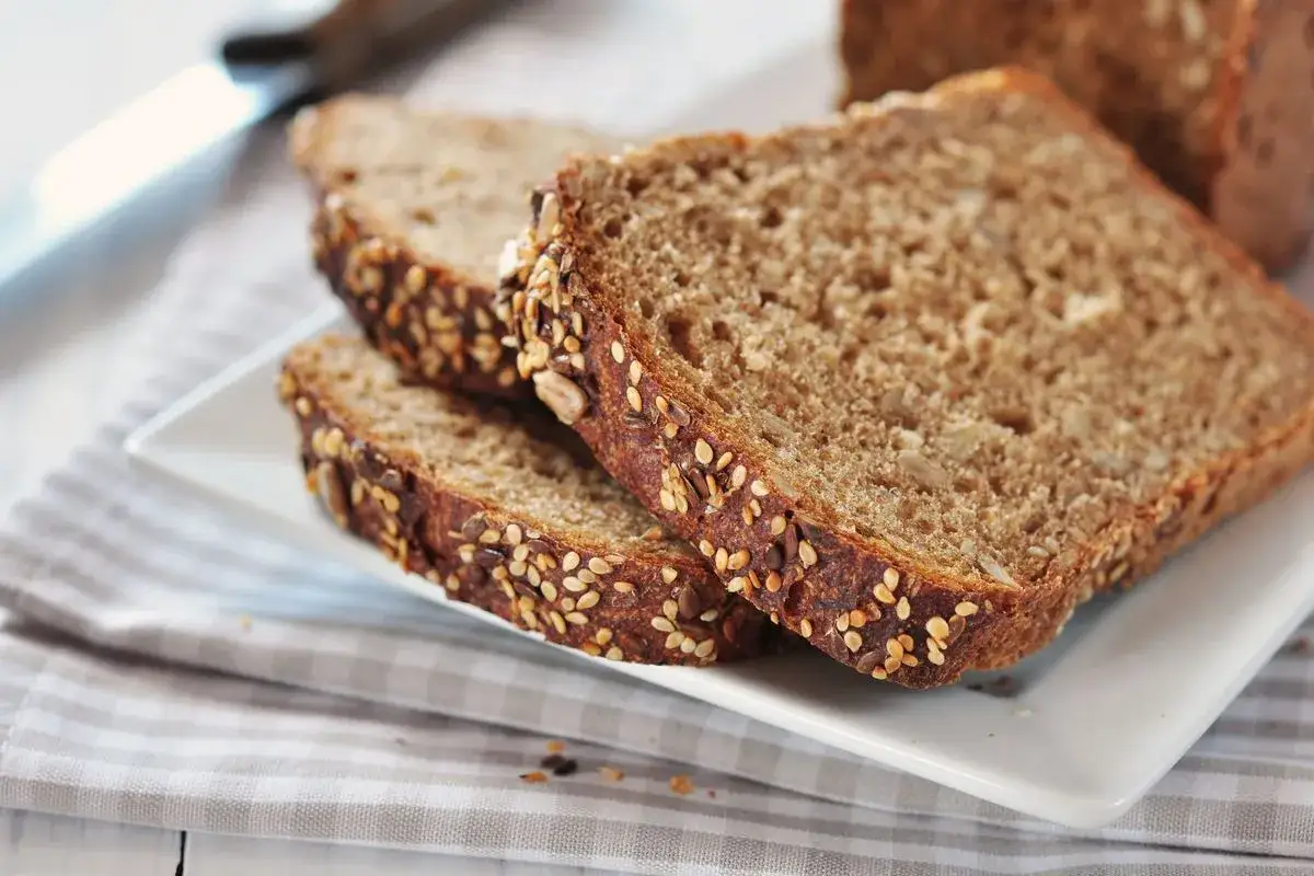 Fette di pane in cassetta fatto in casa, ricche di semi, su un piatto bianco.