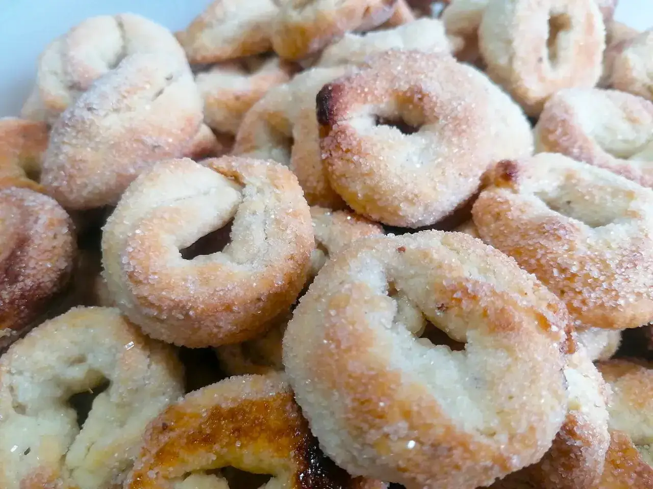 Un primo piano di ciambelline al vino, dolcetti dorati cosparsi di zucchero, pronti per essere gustati.