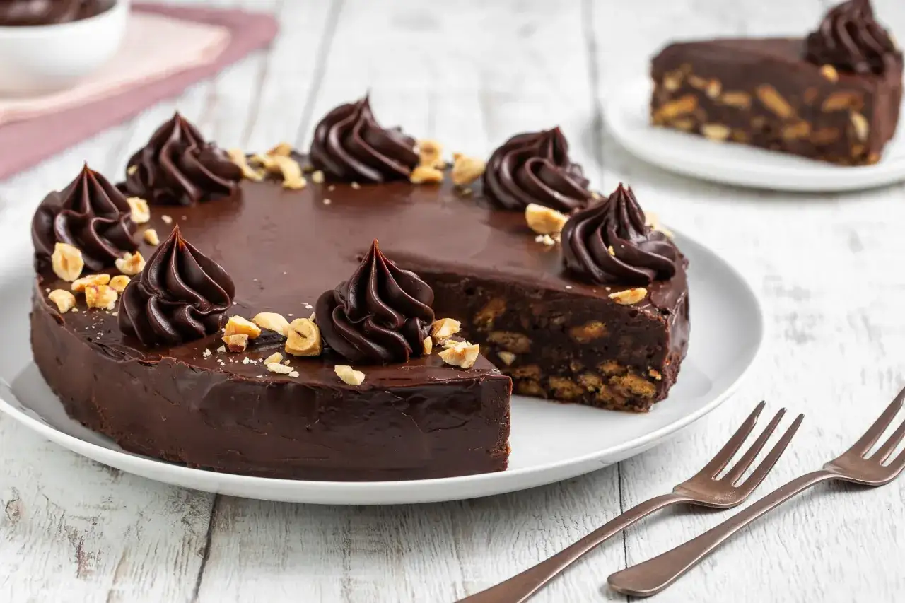 Torta al cioccolato con biscotti e nocciole, decorata con ciuffi di crema e un tocco di salame dolce.