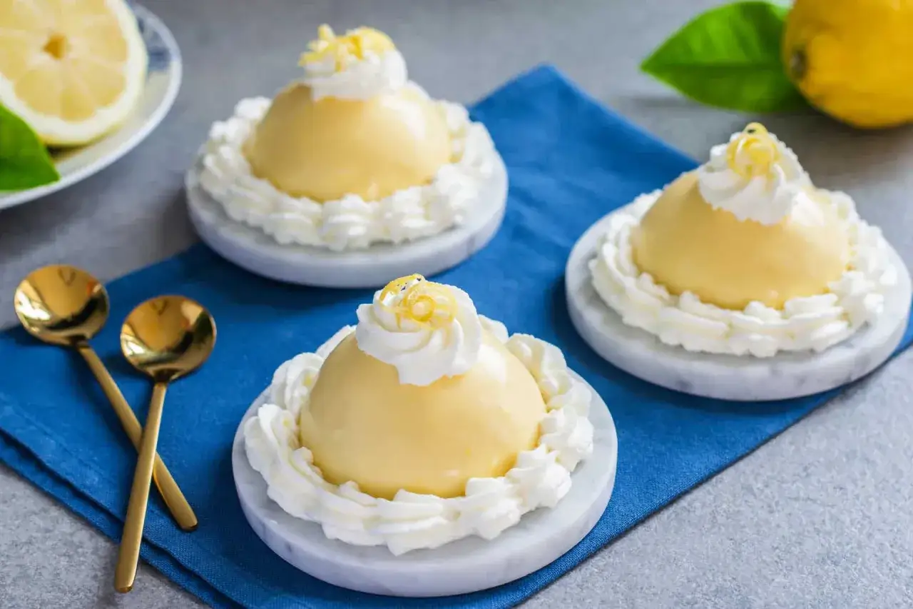 Deliziosi tiramis&ugrave; al limoncello, guarniti con panna montata e scorzette di limone, pronti per essere gustati con cucchiaini dorati.