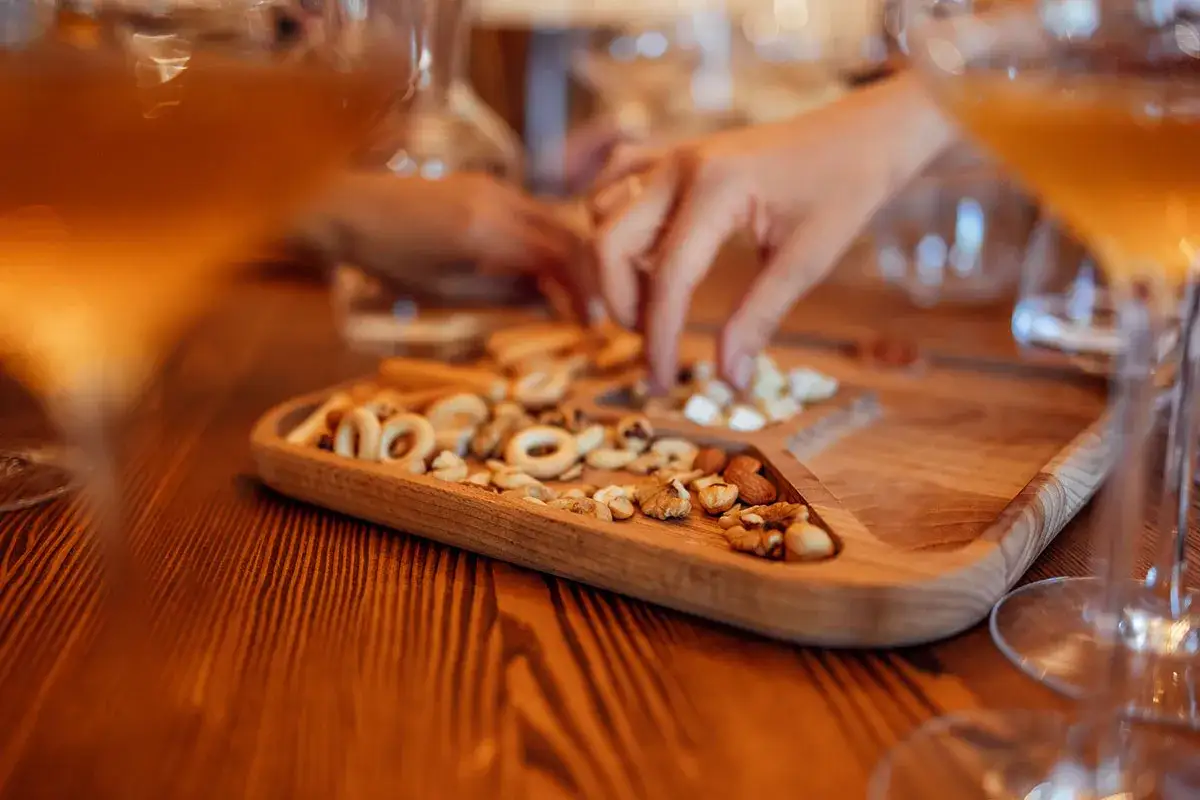 Un vassoio di legno con taralli e frutta secca, accanto a bicchieri di vino ambrato.