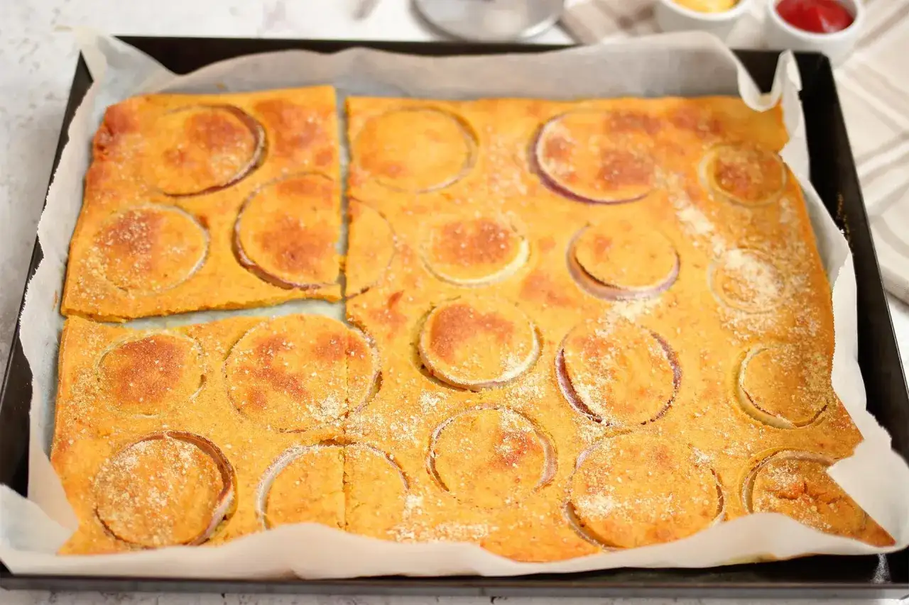 Farinata di ceci appena sfornata, dorata e profumata, con fette di cipolla rossa che creano un disegno invitante. Una ricetta semplice e gustosa.