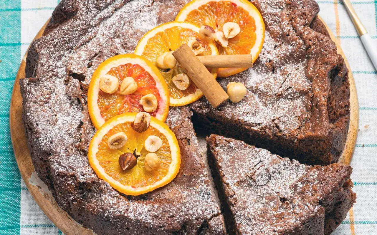 Torta di pane ricetta della nonna, cosparsa di zucchero a velo, decorata con fette d'arancia, nocciole e cannella.