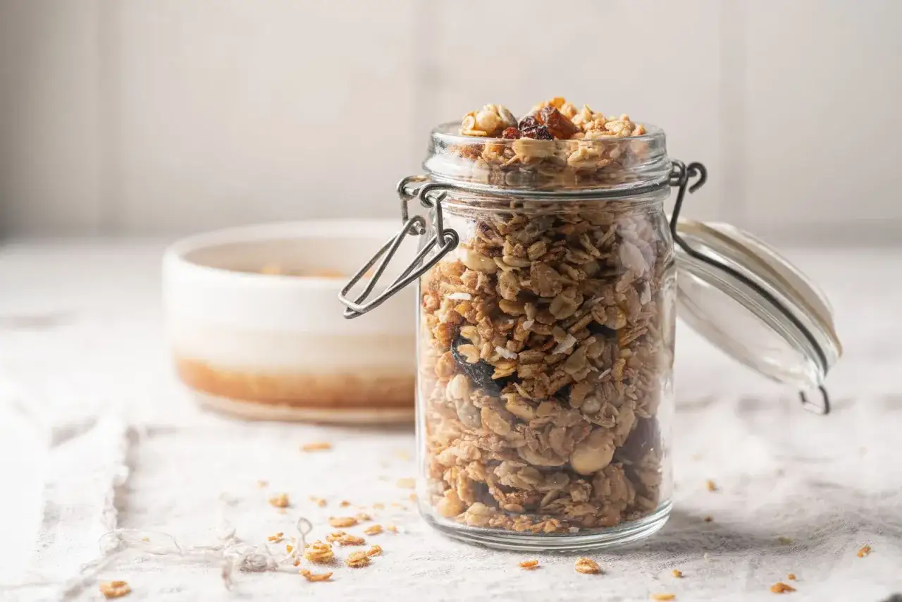 Barattolo di vetro pieno di granola fatta in casa, con fiocchi d'avena, frutta secca e noci.