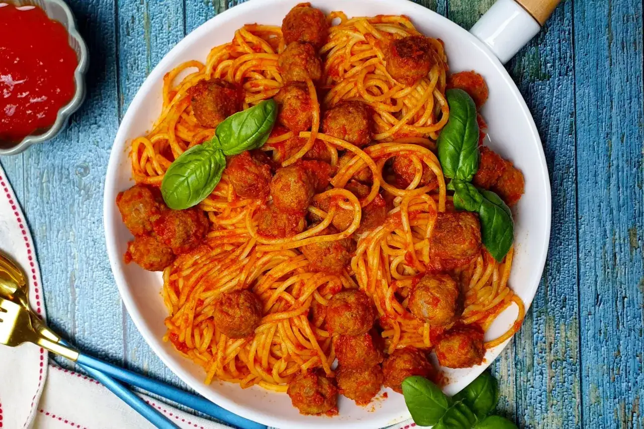 Un piatto invitante di spaghetti con polpette, conditi con sugo rosso e guarniti con foglie di basilico fresco.