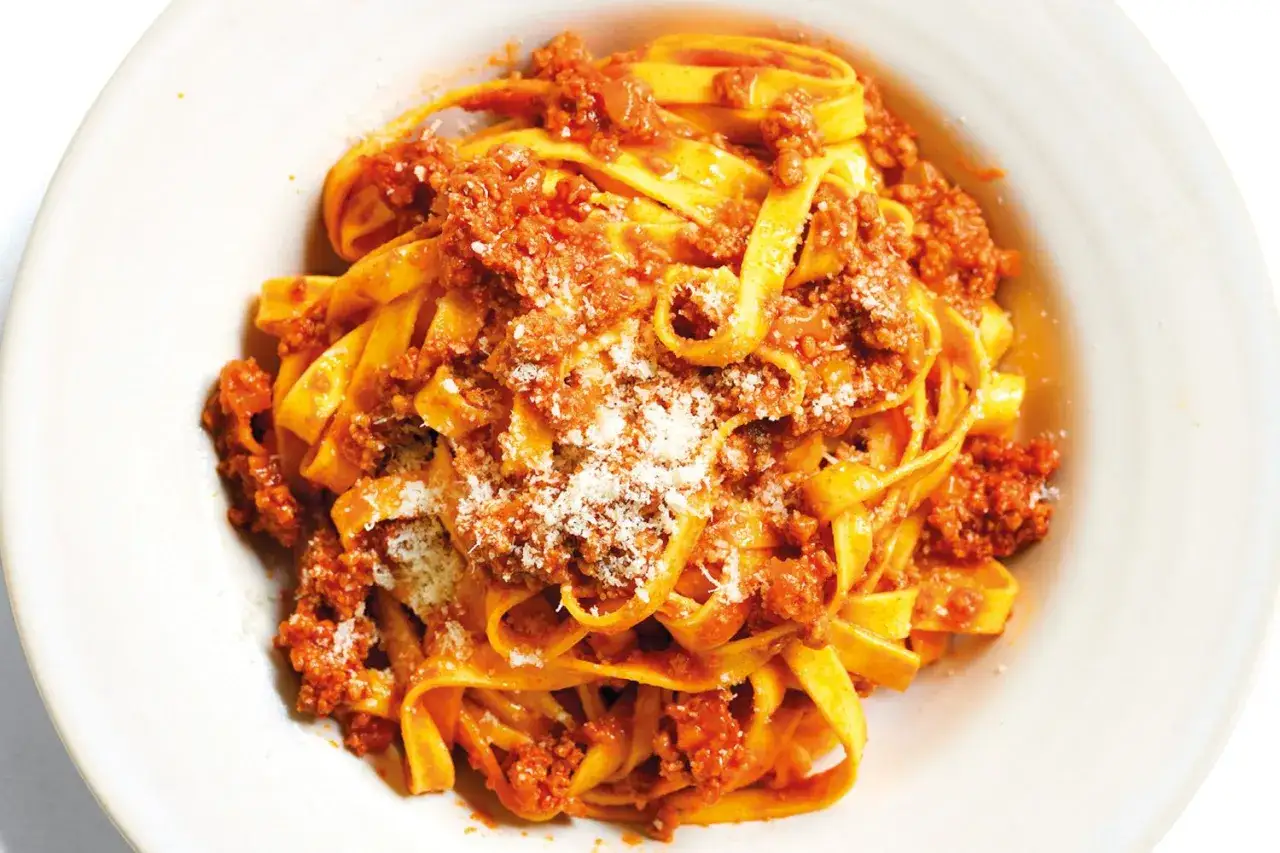 Un piatto invitante di tagliatelle al ragù, condite con abbondante sugo di carne e una spolverata di parmigiano.