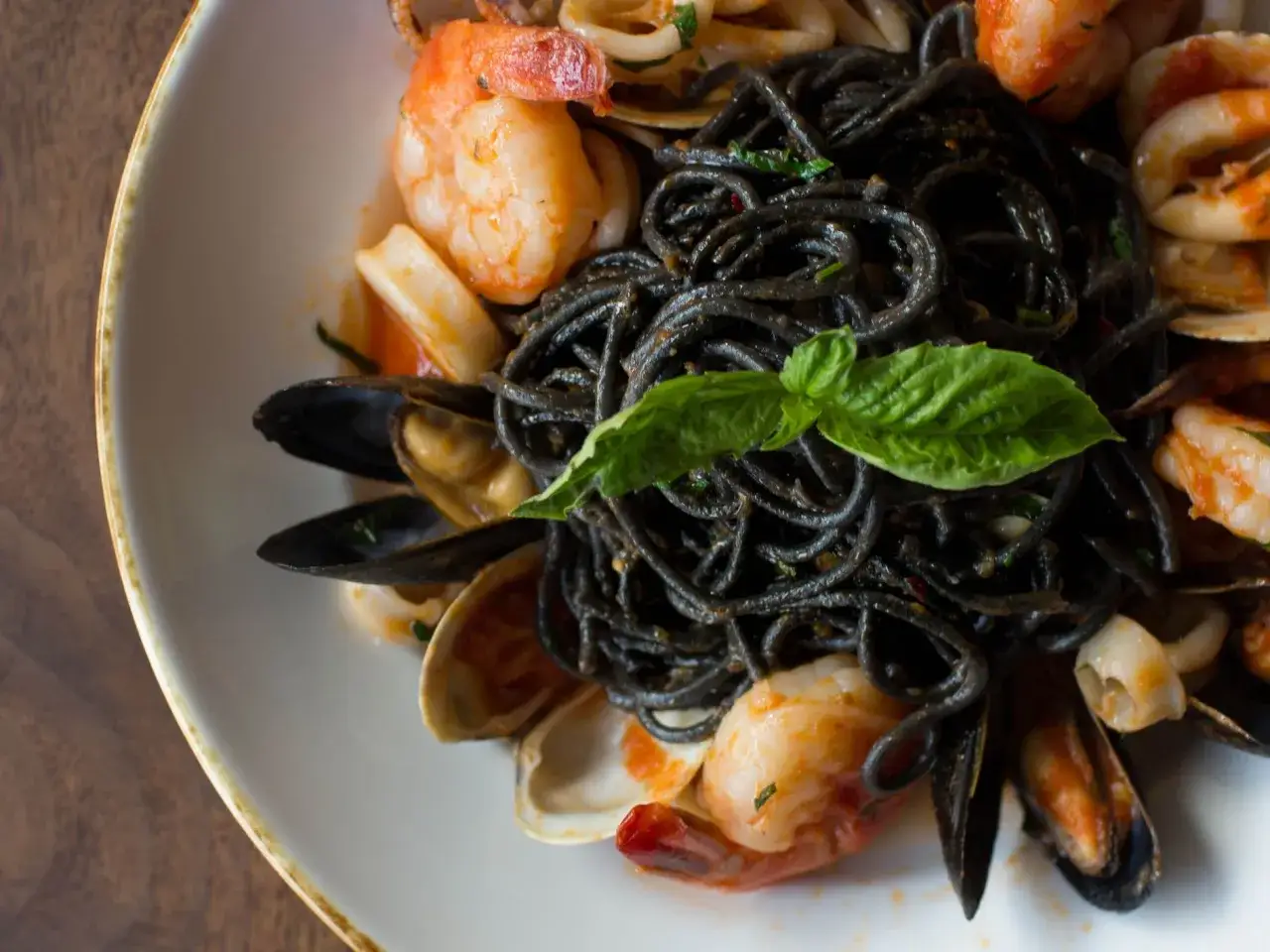 Spaghetti al nero di seppia con gamberi, cozze e vongole, guarniti con basilico fresco. Un piatto di mare invitante.