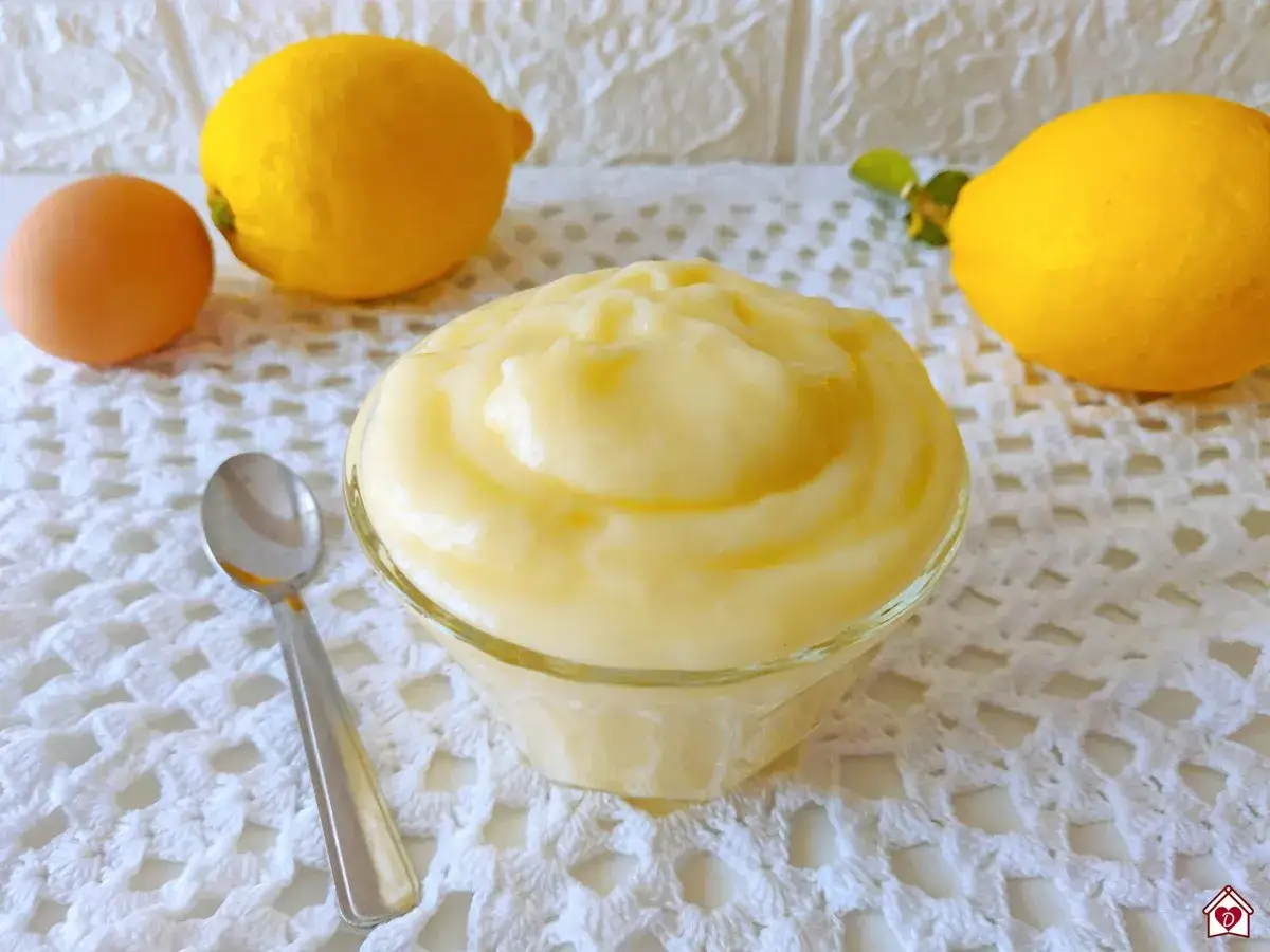 Crema pasticcera ricetta della nonna in una ciotola, con uovo e limoni sullo sfondo.