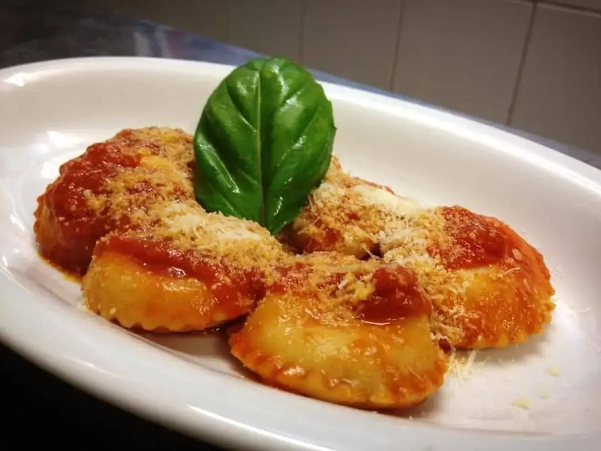 Ravioli Capresi fumanti, conditi con sugo rosso e parmigiano, guarniti da una foglia di basilico fresco.