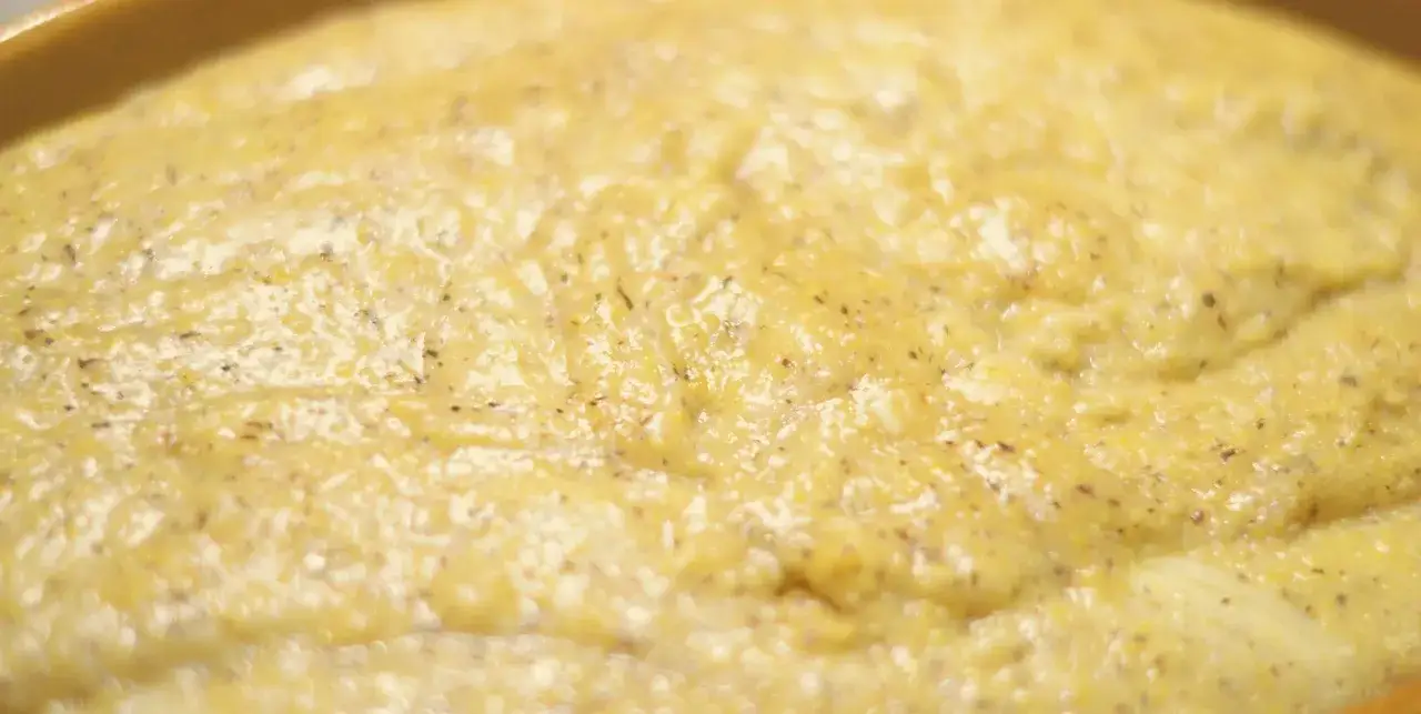 Polenta taragna cremosa, con il suo colore dorato e i puntini scuri delle erbe aromatiche, pronta per essere gustata.