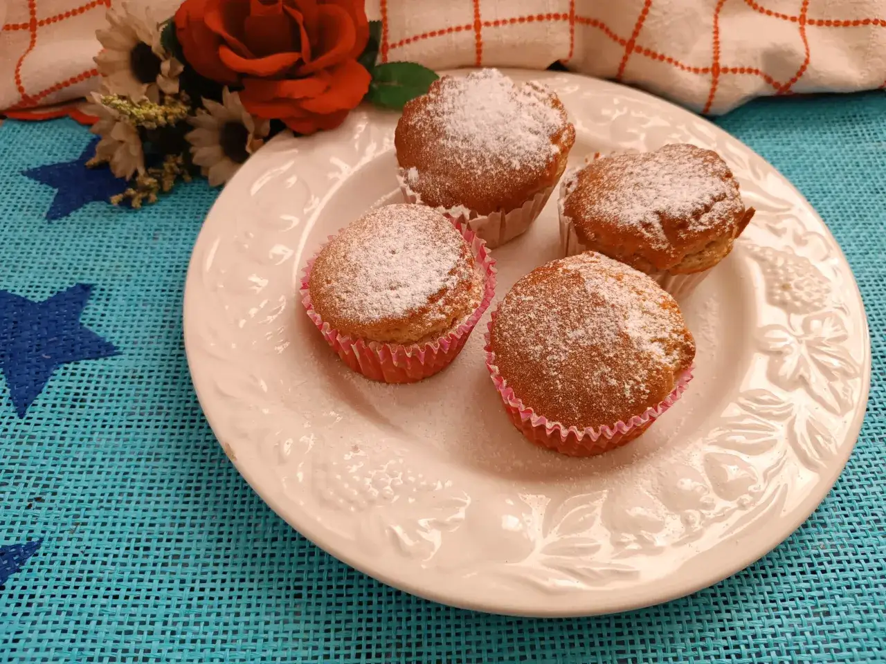 Quattro muffin in friggitrice ad aria, spolverati di zucchero a velo, su un piatto bianco. Perfetti con una colazione leggera a base di yogurt.
