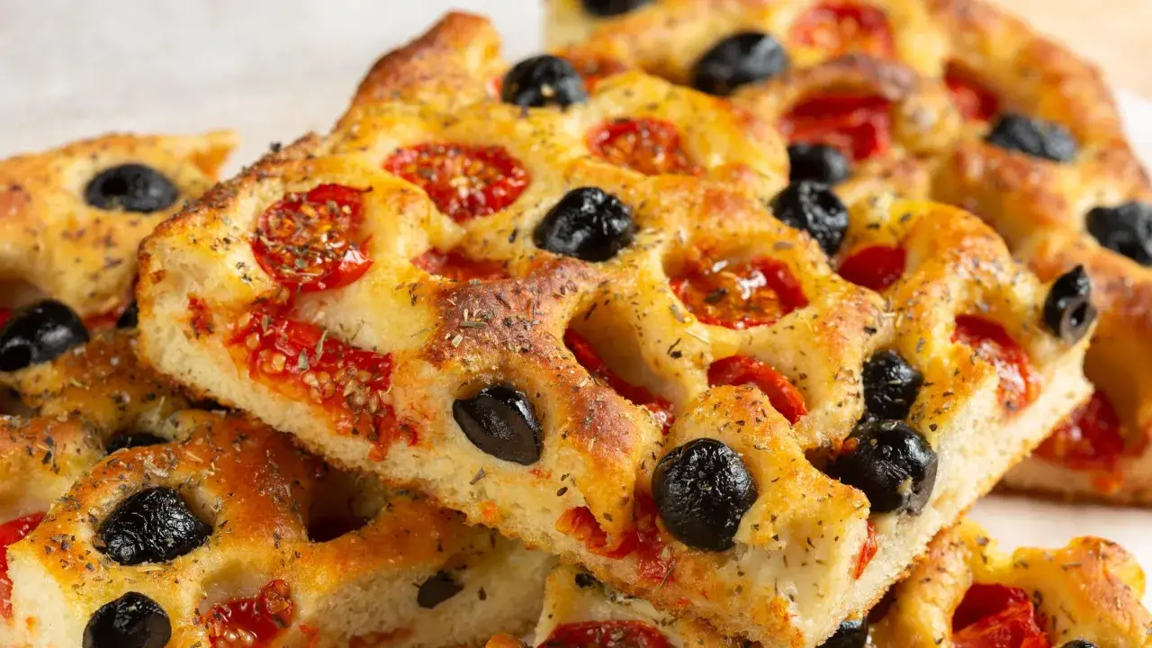Focaccia pugliese dorata, con pomodorini succosi e olive nere, cosparsa di erbe aromatiche.