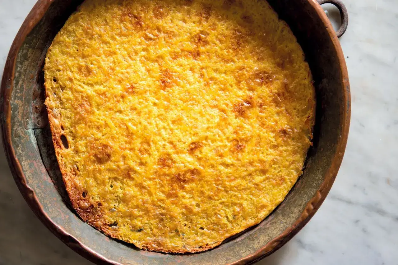Farinata di ceci appena sfornata in una padella di rame, dorata e croccante sui bordi.