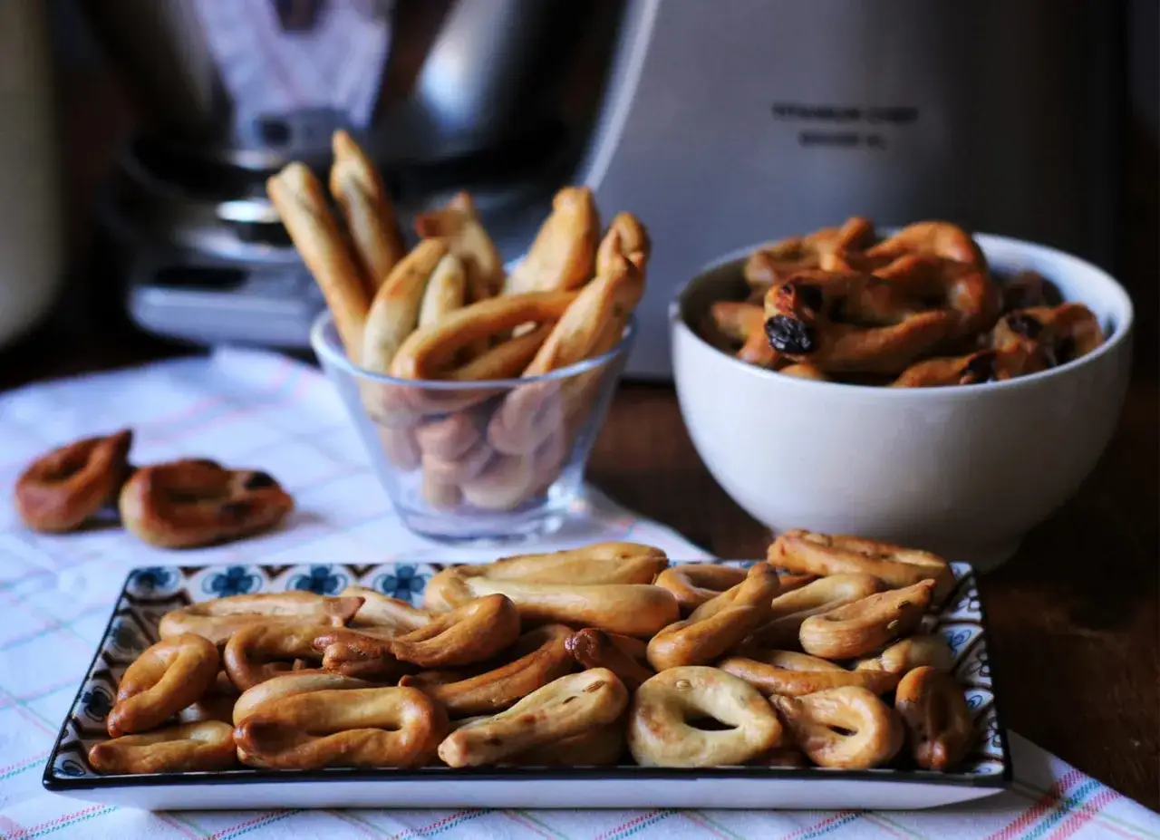 Taralli al vino bianco dorati e croccanti, alcuni in ciotole, altri su un piatto decorato, pronti per essere gustati.