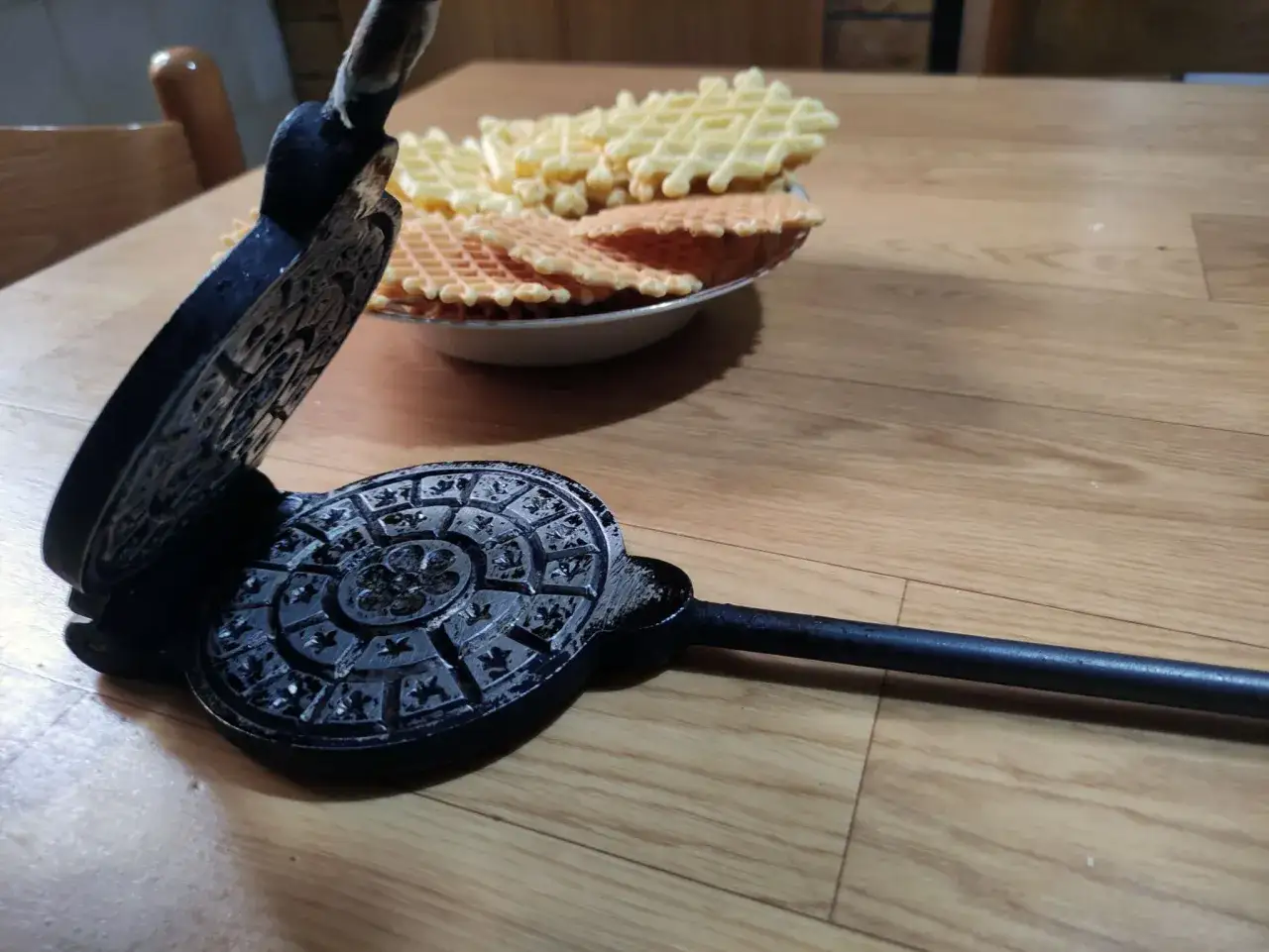 Vecchia piastra per ferratelle abruzzesi, con dolci appena sfornati in un piatto.