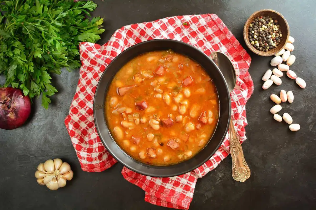 Una ciotola fumante di sagne e fagioli, con contorno di prezzemolo, cipolla rossa e aglio.
