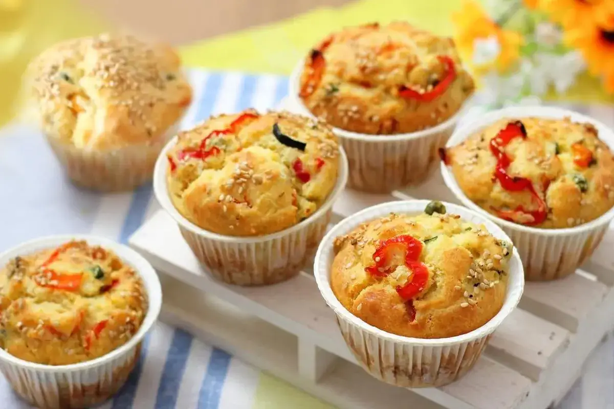 Muffin salati dorati con peperoni rossi, zucchine e semi di sesamo, perfetti per uno spuntino gustoso.