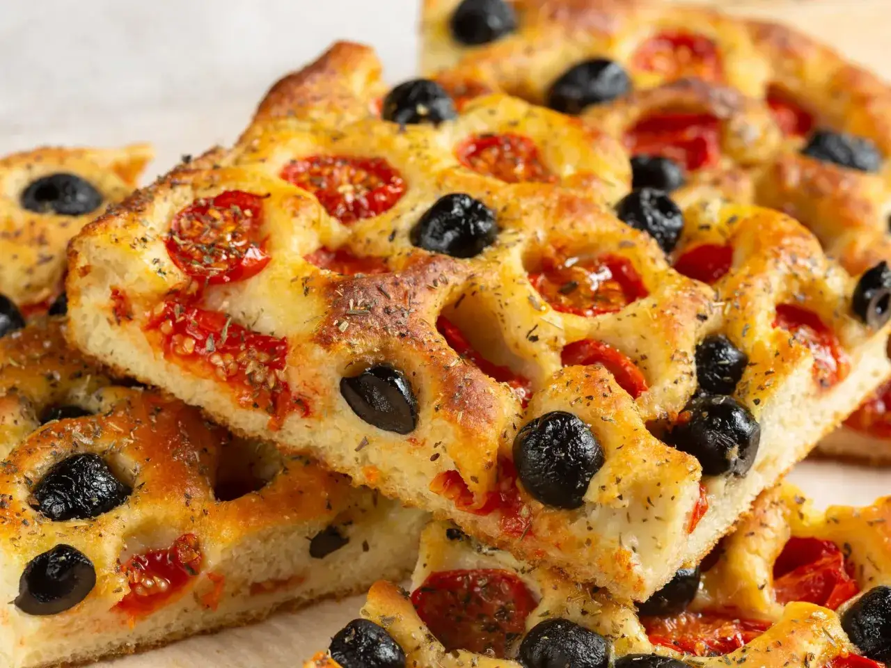 Focaccia barese soffice e dorata, con pomodorini succosi e olive nere, condita con erbe aromatiche.