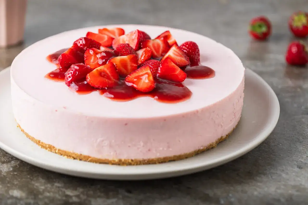 Delizioso cheesecake alle fragole, con fragole fresche e salsa rossa, su un piatto bianco.