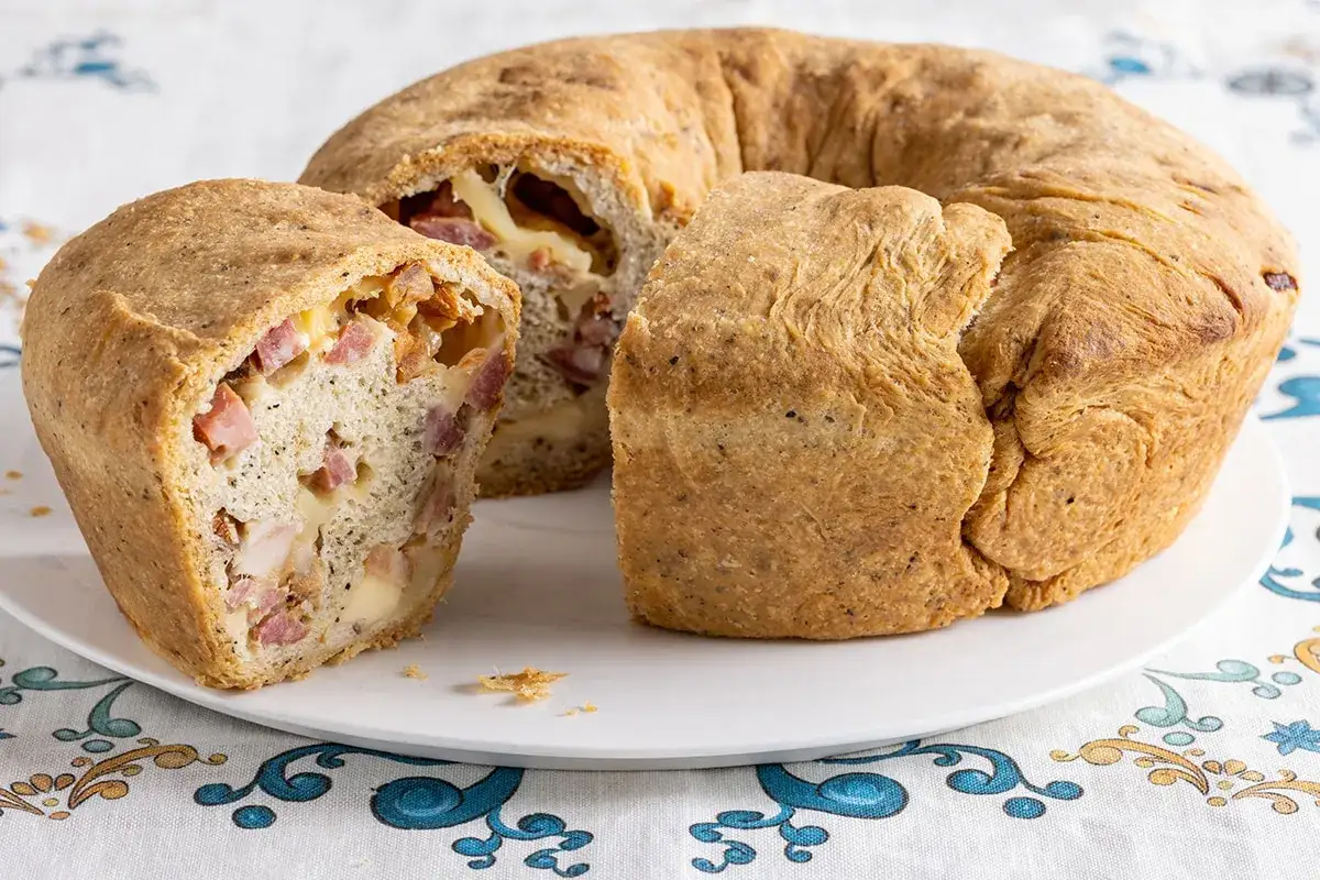 Un casatiello napoletano, un anello di pane dorato farcito con salumi e formaggio, tagliato per mostrarne il ripieno invitante.