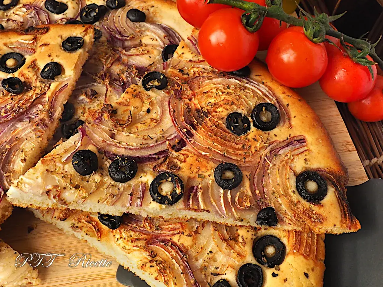 Focaccia con cipolle rosse e olive nere, dorata e fragrante, con pomodorini freschi a lato.