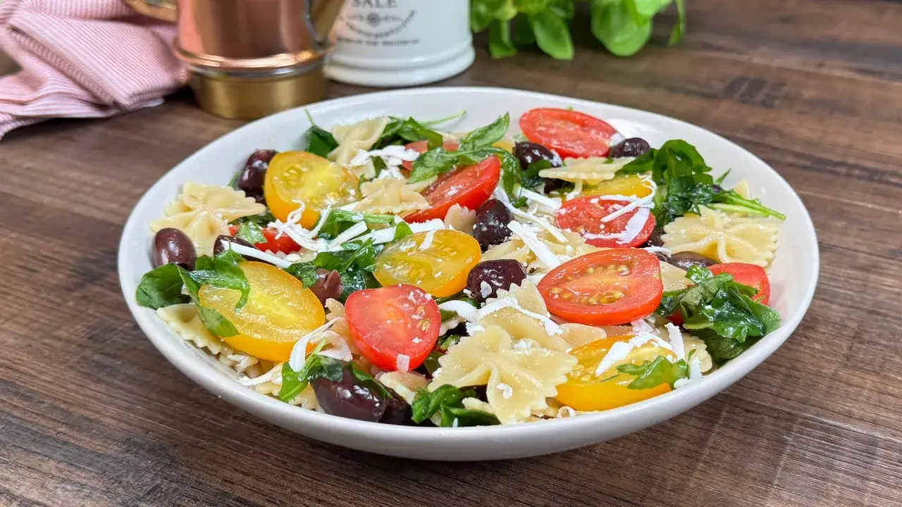 Insalata di pasta crudaiola con farfalle, pomodorini colorati, olive nere e formaggio grattugiato.