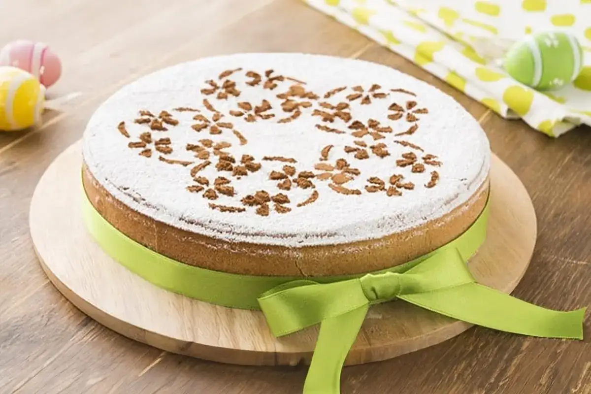 Deliziosa cassata al forno con decorazioni floreali in cacao e zucchero a velo, legata da un nastro verde. Perfetta per la Pasqua.