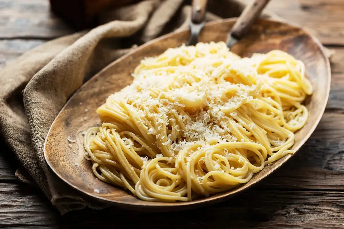 Un piatto di spaghetti in bianco, conditi con abbondante parmigiano grattugiato, serviti su un tagliere di legno rustico.