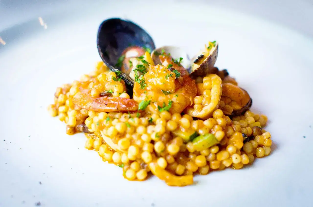 Fregola con pesce: pasta sarda con gamberi, cozze e vongole, un piatto gustoso e colorato.