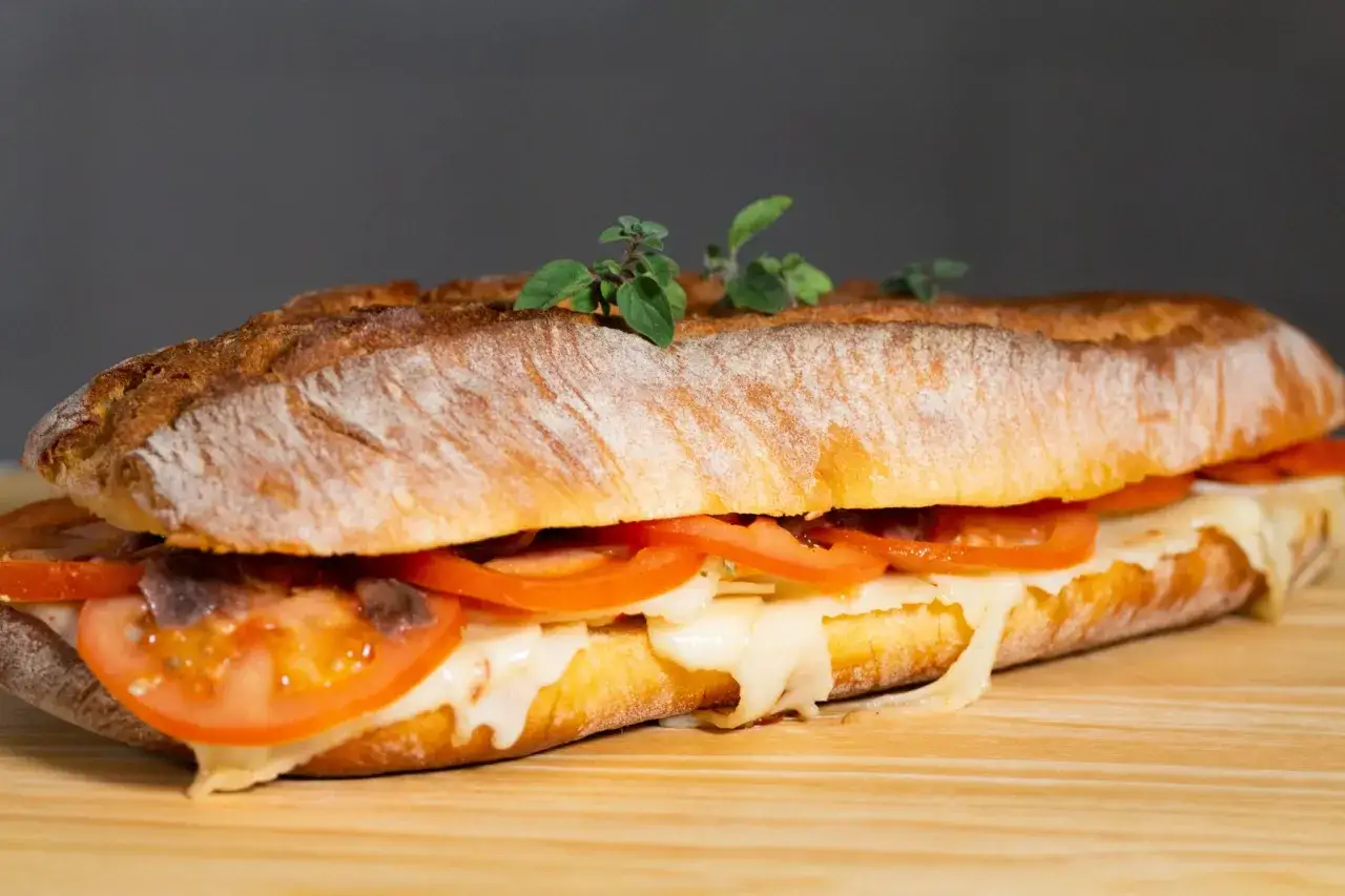 Pane cunzato: un panino croccante con pomodoro, formaggio filante e acciughe, guarnito con erbe aromatiche fresche.