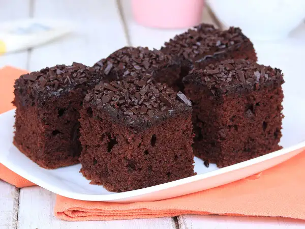 Quattro fette di torta al cioccolato morbida e umida, ricoperte di codette di cioccolato, su un piatto bianco.