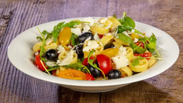 Pasta crudaiola colorata con pomodorini, olive nere, rucola e scaglie di parmigiano. Fresca e invitante.