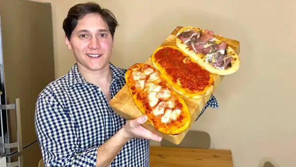 Uomo sorridente mostra tre lingue di pizza senza lievito: una margherita, una al pomodoro e una con prosciutto e funghi.