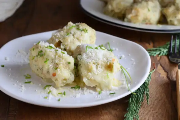 Tre gnocchi di pane soffici e dorati, cosparsi di parmigiano grattugiato e erba cipollina fresca, su un piatto bianco.