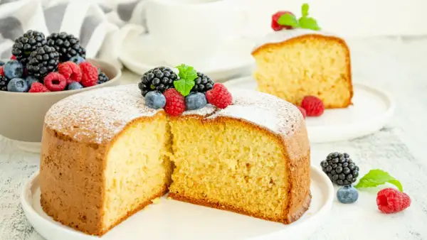 Torta soffice allo yogurt greco, decorata con frutti di bosco freschi e una spolverata di zucchero a velo.