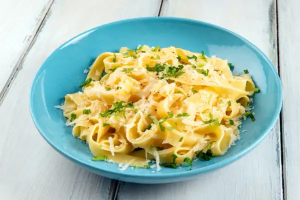 Un piatto di pasta burro e parmigiano, condita con prezzemolo fresco, servita in una ciotola blu su un tavolo di legno.