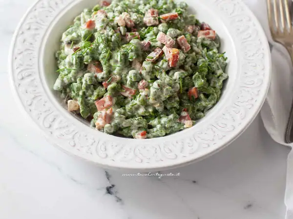Un piatto di gnocchetti tirolesi verdi, conditi con panna, piselli e speck croccante, guarniti con erba cipollina.