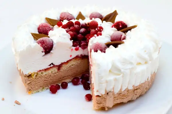 Torta gelato a strati con panna montata, frutti rossi e cioccolato. Una fetta è stata tagliata, rivelando il suo interno goloso.