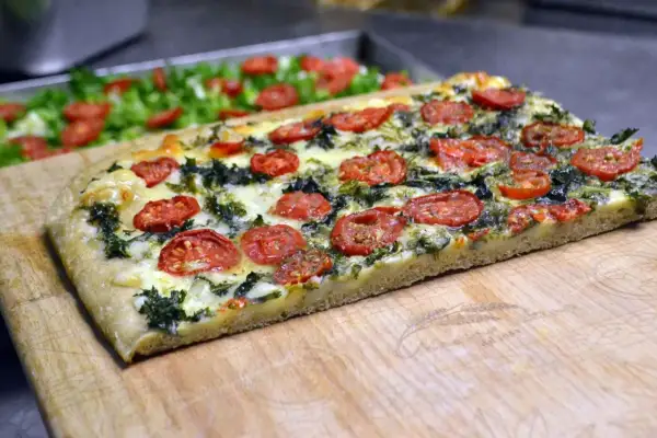 Focaccia messinese con pomodorini e verdure, un sapore autentico su un tagliere di legno.