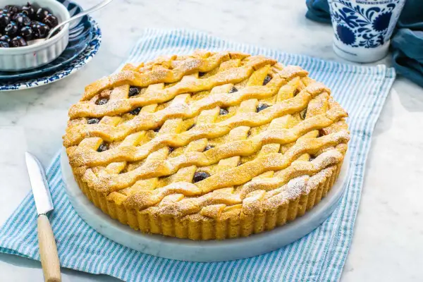 Una deliziosa crostata amalfitana con una griglia dorata di pasta frolla, cosparsa di zucchero a velo e ripiena di amarene.