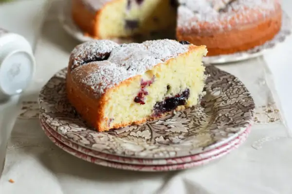 Una fetta di torta nua soffice, cosparsa di zucchero a velo, con un cuore di marmellata di frutti di bosco.
