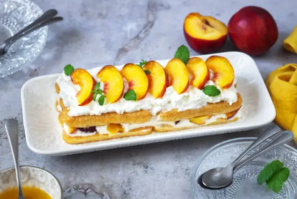 Delizioso tiramisù alle pesche, con strati di savoiardi, crema soffice e pesche fresche, guarnito con menta.