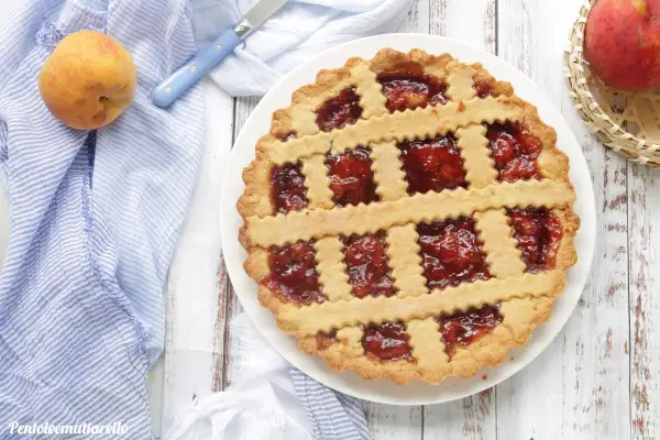 Deliziosa crostata di pesche con ripieno rosso brillante, decorata con strisce di pasta frolla a zig-zag.