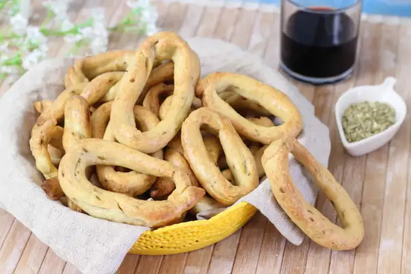 Taralli al finocchietto con lievito, croccanti e profumati, in un cestino con un bicchiere di vino rosso e semi di finocchio.
