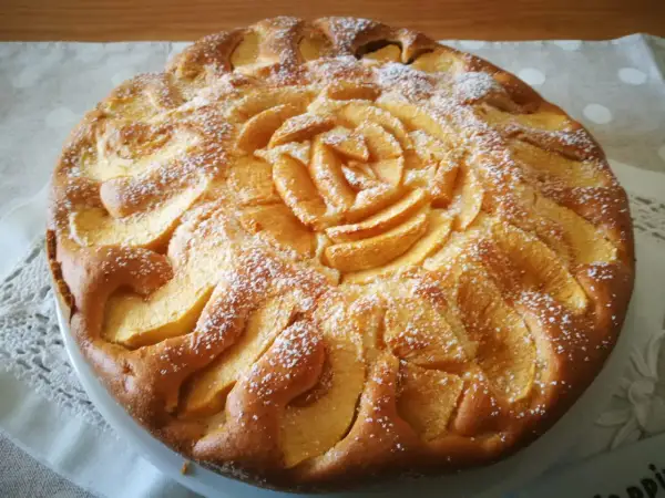 Deliziosa torta di mele senza glutine, con mele disposte a rosa al centro e spolverata di zucchero a velo.