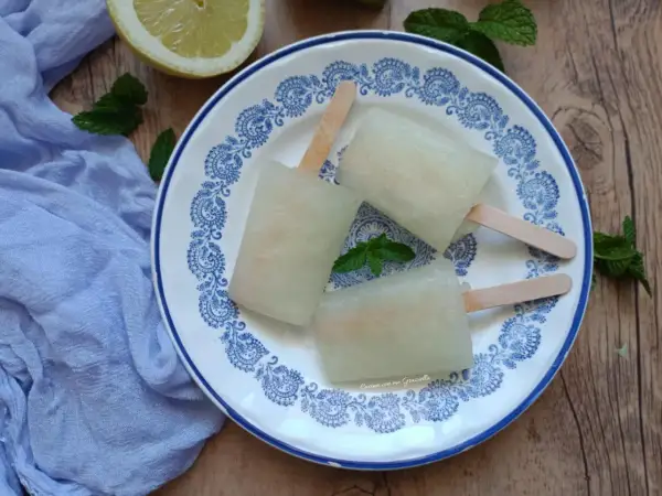 Tre ghiaccioli al limone fatti in casa su un piatto decorato, con limone e menta fresca. Perfetti per un'estate rinfrescante.